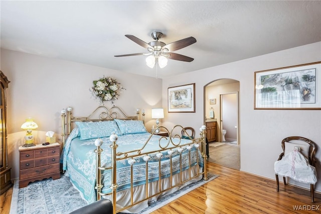 bedroom with ensuite bathroom, wood finished floors, arched walkways, and ceiling fan