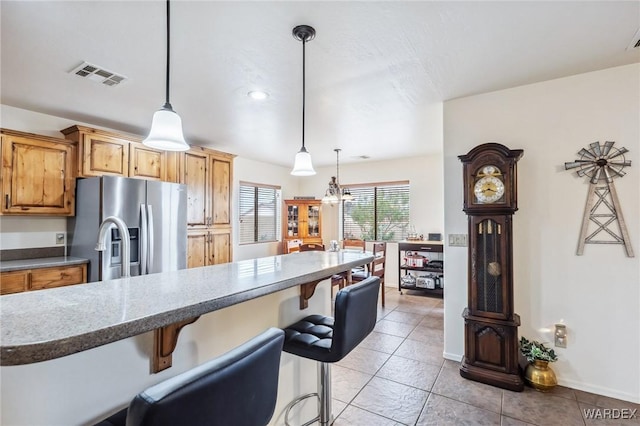 kitchen with a breakfast bar, stainless steel fridge, visible vents, and light tile patterned floors