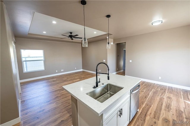 kitchen with pendant lighting, light wood finished floors, stainless steel dishwasher, a sink, and baseboards