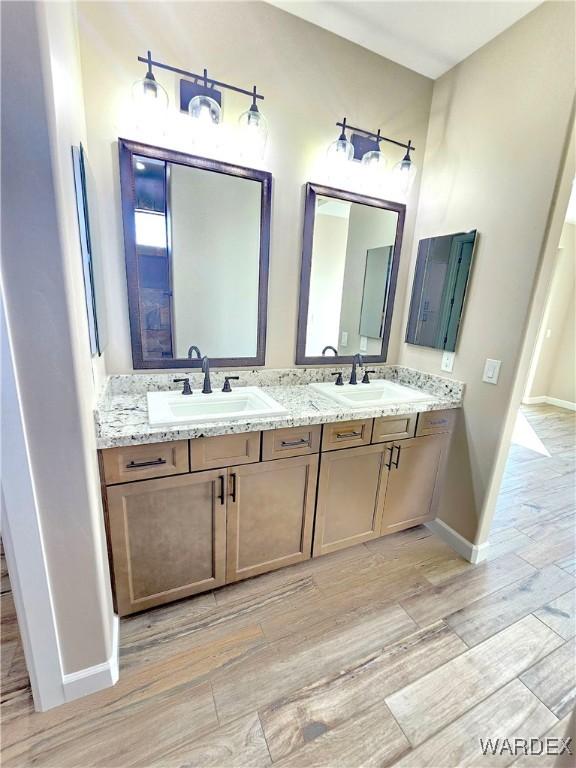 full bath with double vanity, a sink, and wood finished floors