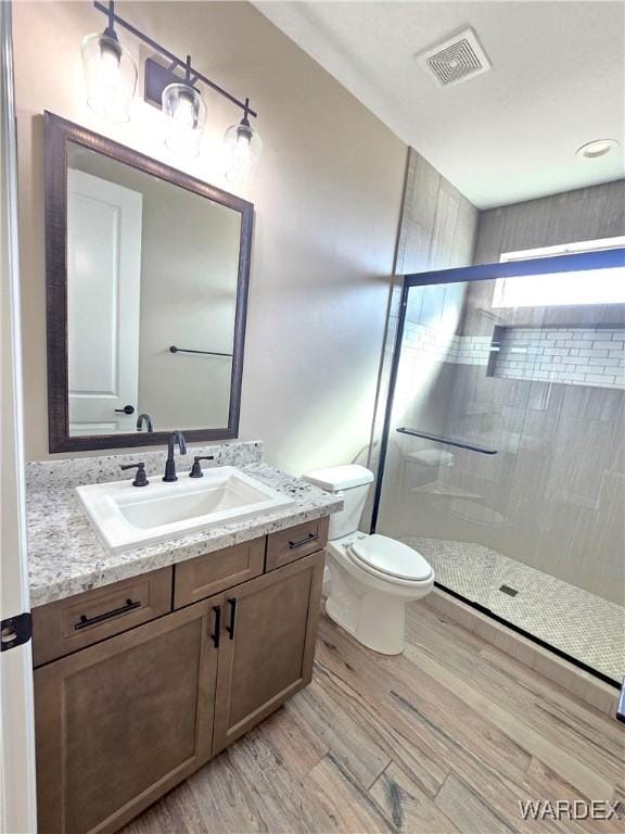 bathroom featuring toilet, wood finished floors, vanity, visible vents, and a shower stall