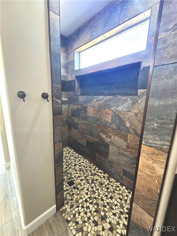 full bath featuring tiled shower, wood finished floors, and baseboards