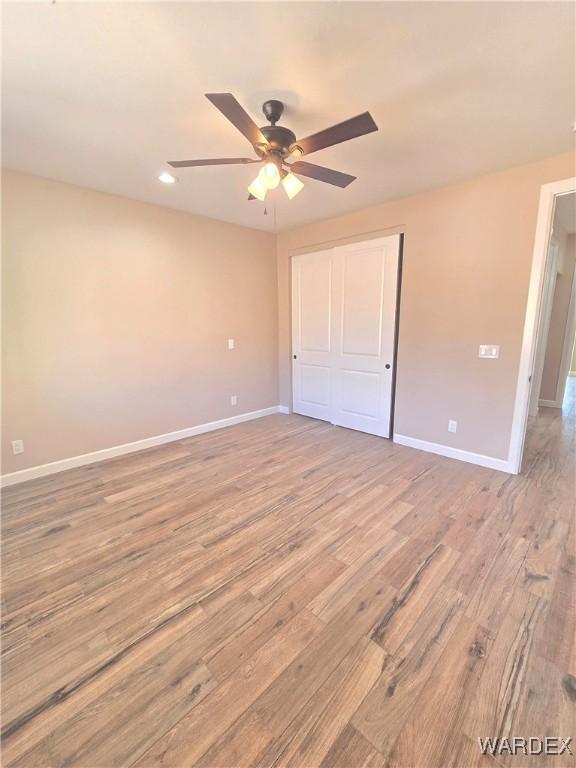 unfurnished bedroom with light wood-type flooring, a closet, ceiling fan, and baseboards