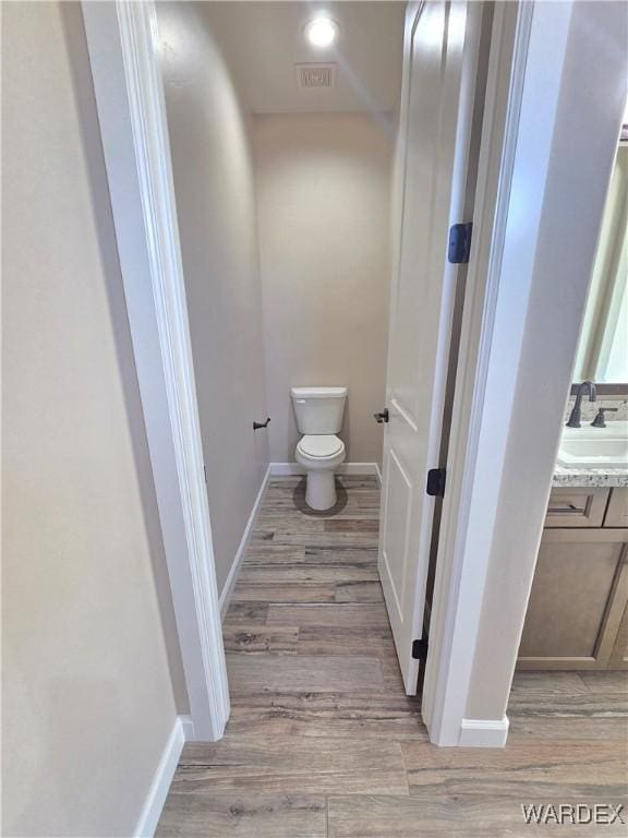 bathroom featuring toilet, wood finished floors, visible vents, a sink, and baseboards