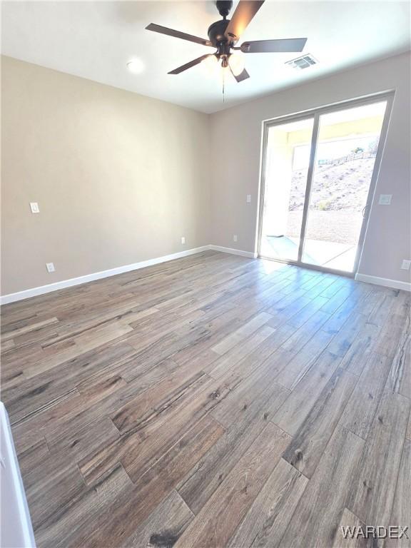 spare room with a ceiling fan, visible vents, baseboards, and wood finished floors