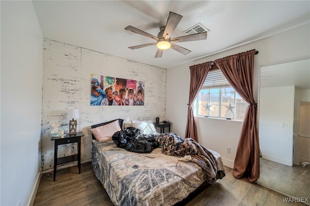 bedroom featuring a ceiling fan, visible vents, baseboards, and wood finished floors