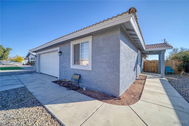 view of home's exterior with concrete driveway, a tile roof, an attached garage, fence, and stucco siding