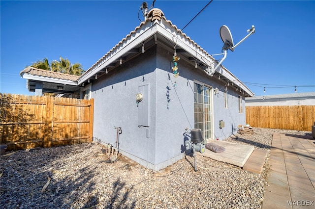 view of side of home featuring a tiled roof, fence, and stucco siding