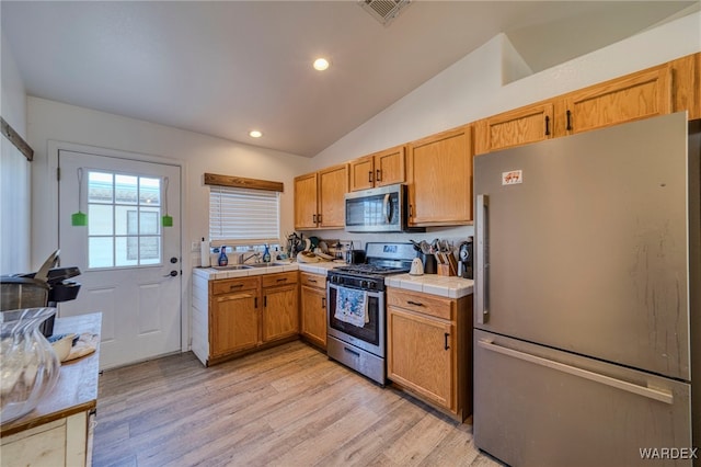 kitchen with lofted ceiling, stainless steel appliances, visible vents, tile counters, and light wood finished floors