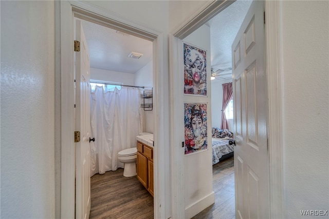 ensuite bathroom with toilet, a shower with shower curtain, wood finished floors, visible vents, and vanity