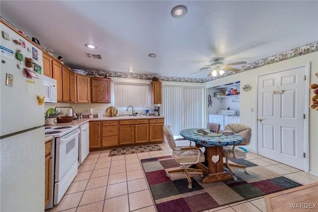 kitchen featuring brown cabinets, washing machine and clothes dryer, light tile patterned floors, light countertops, and white appliances