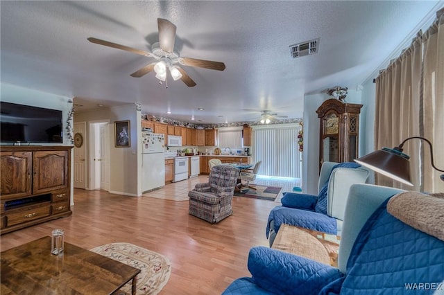 living room featuring light wood-style floors, a ceiling fan, visible vents, and a textured ceiling