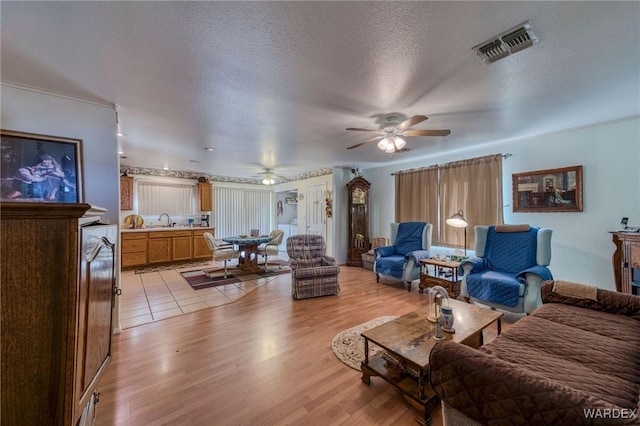 living room featuring a textured ceiling, visible vents, a ceiling fan, a wealth of natural light, and light wood finished floors