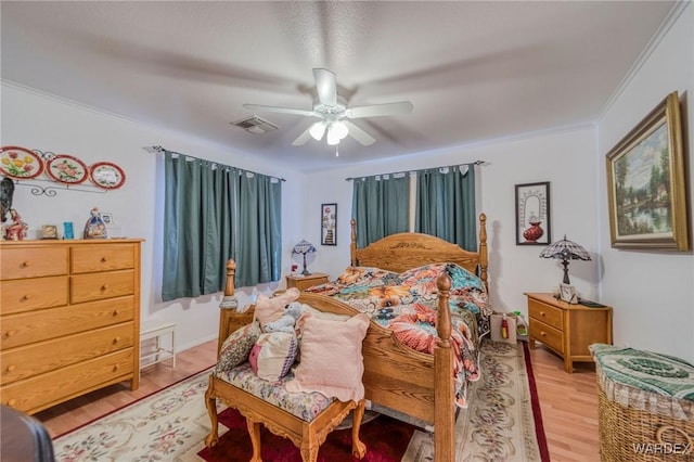 bedroom featuring ornamental molding, light wood-type flooring, visible vents, and ceiling fan