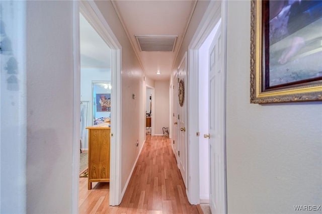 hall featuring light wood-style floors, visible vents, crown molding, and baseboards