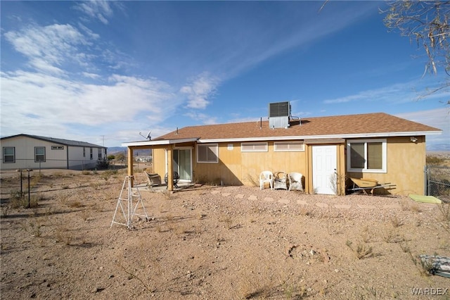 rear view of house featuring fence, cooling unit, and roof with shingles