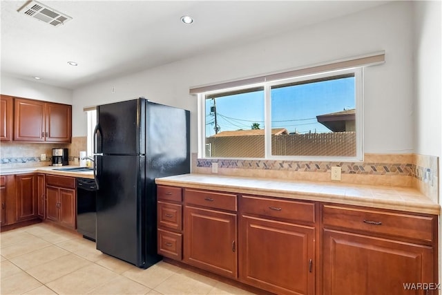 kitchen with light tile patterned floors, visible vents, tile counters, black appliances, and tasteful backsplash