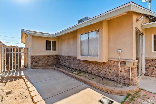 view of side of home with stone siding, a patio, fence, and stucco siding