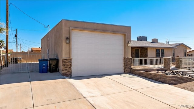 view of front of house with stone siding, concrete driveway, fence, and stucco siding