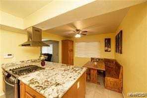 kitchen with a ceiling fan, light stone counters, range hood, light tile patterned flooring, and gas range