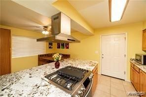 kitchen with stainless steel microwave, light tile patterned flooring, brown cabinetry, island range hood, and stove