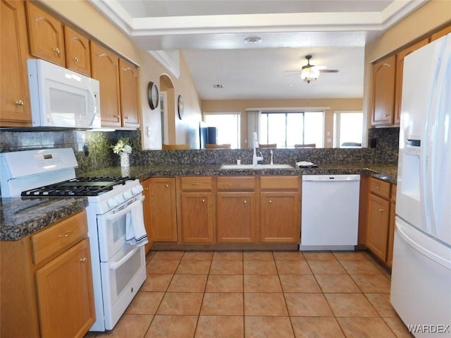 kitchen with white appliances, light tile patterned floors, brown cabinetry, a peninsula, and a sink