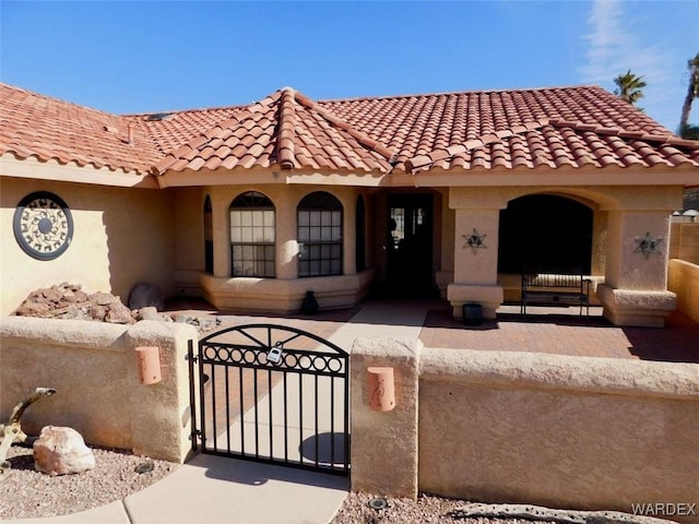 mediterranean / spanish-style home with a fenced front yard, a gate, and a tile roof