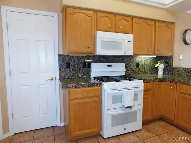 kitchen with dark stone counters, white appliances, light tile patterned flooring, and decorative backsplash