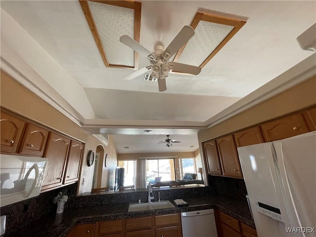 kitchen with white appliances, a sink, visible vents, brown cabinetry, and dark countertops