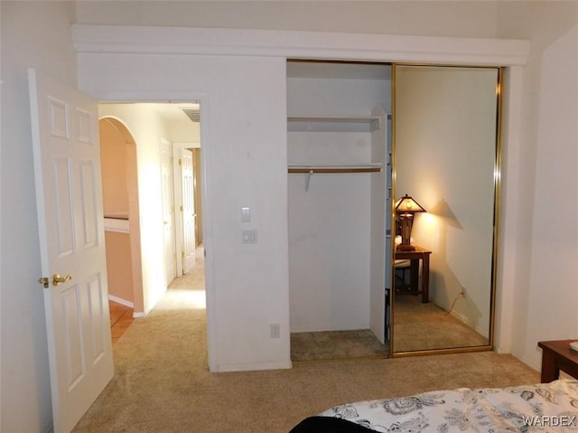 bedroom featuring light carpet, arched walkways, and a closet