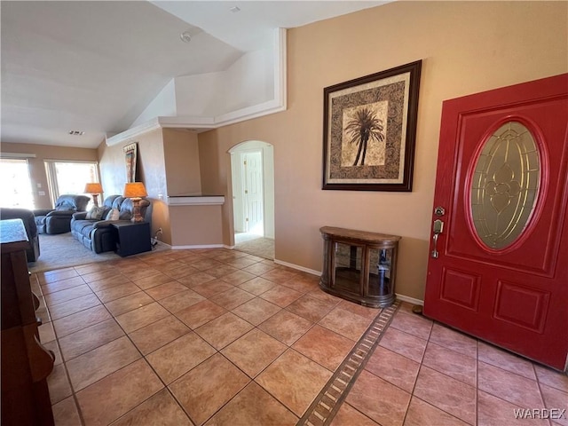 entryway featuring arched walkways, light tile patterned flooring, lofted ceiling, and baseboards