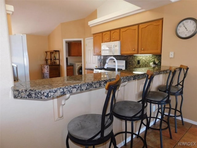 kitchen with a peninsula, white appliances, a breakfast bar area, and washer / dryer