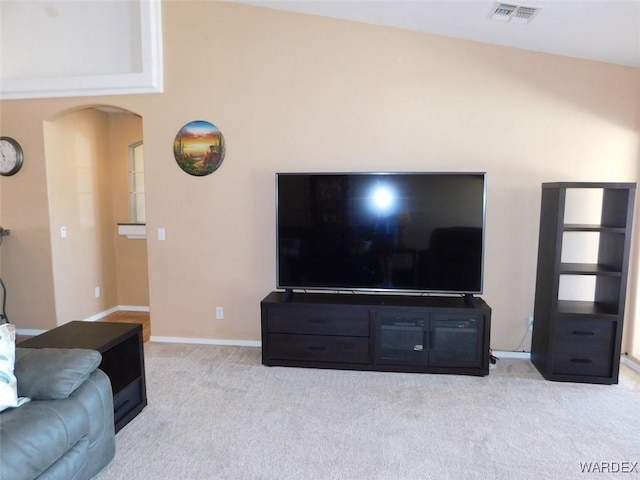 living area with arched walkways, baseboards, visible vents, and light colored carpet