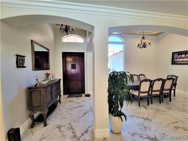 entryway with baseboards, arched walkways, marble finish floor, crown molding, and a notable chandelier