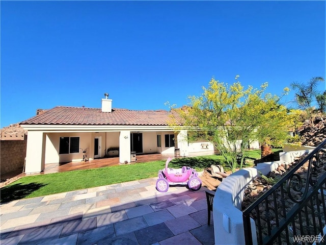 rear view of property with a patio area, a tiled roof, a chimney, and stucco siding