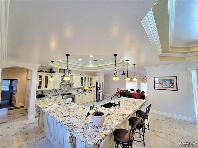 kitchen featuring arched walkways, glass insert cabinets, hanging light fixtures, a tray ceiling, and a large island with sink