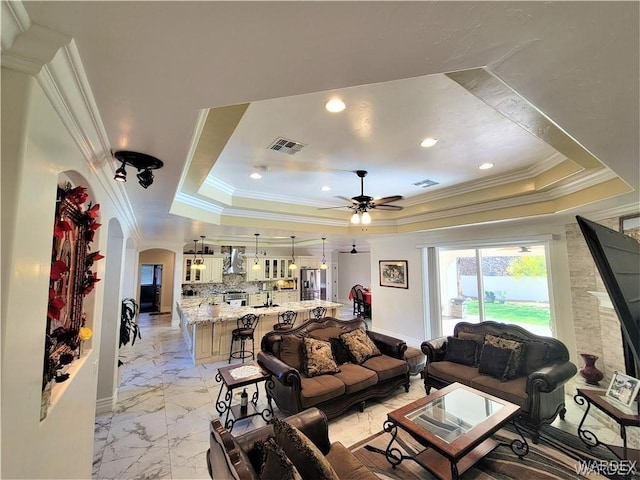 living area with arched walkways, a raised ceiling, and visible vents