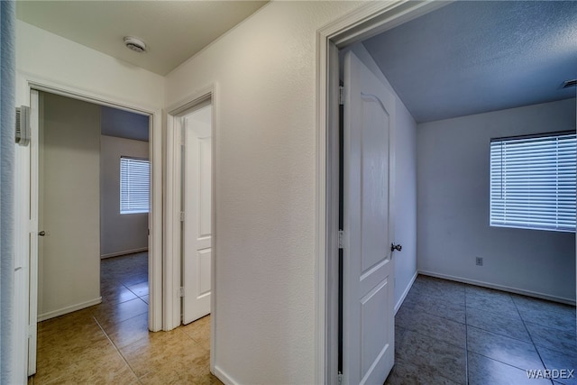 corridor with light tile patterned floors, plenty of natural light, visible vents, and baseboards