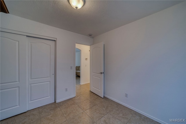 unfurnished bedroom featuring a textured ceiling, light tile patterned floors, a closet, and baseboards