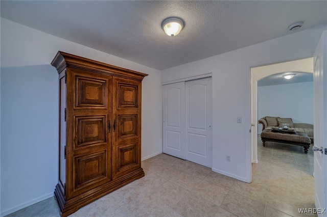 bedroom with arched walkways, a closet, a textured ceiling, and baseboards