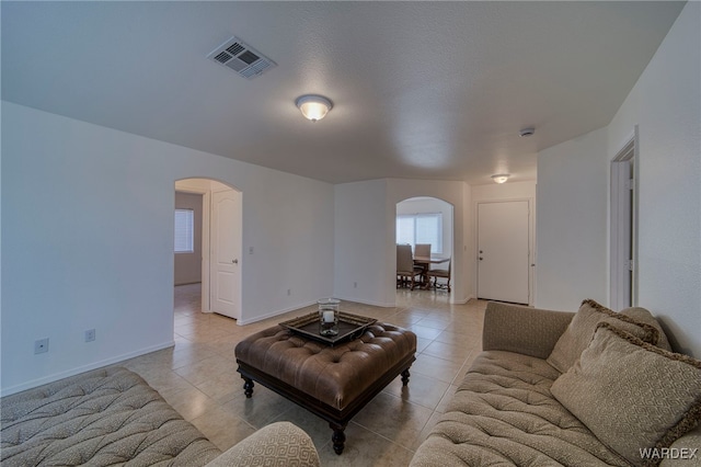 living room with light tile patterned floors, baseboards, visible vents, and arched walkways