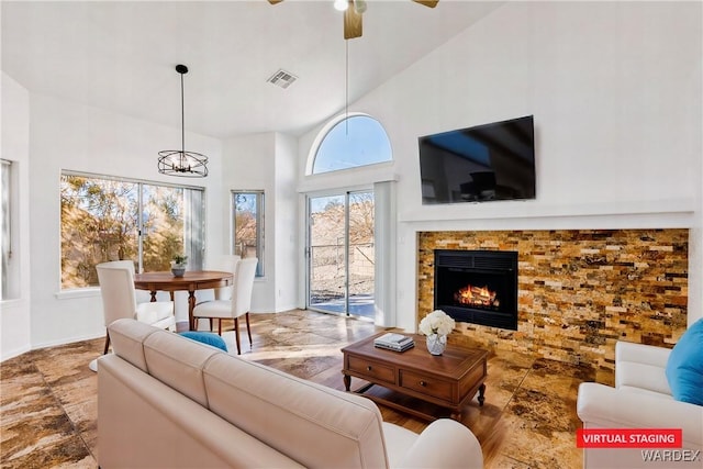 living room featuring a warm lit fireplace, baseboards, visible vents, a towering ceiling, and ceiling fan with notable chandelier