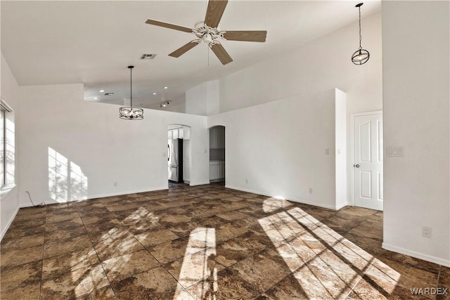 empty room with visible vents, arched walkways, baseboards, a towering ceiling, and ceiling fan