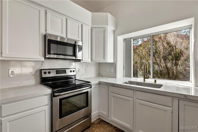 kitchen featuring stainless steel appliances, a sink, white cabinetry, and light stone countertops