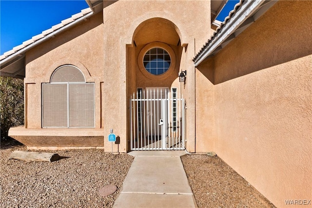 property entrance with a gate, a tile roof, and stucco siding