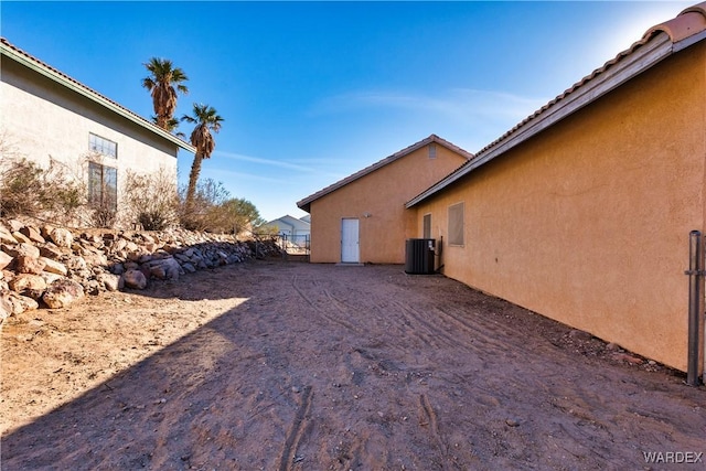 view of side of home with central AC unit, fence, and stucco siding