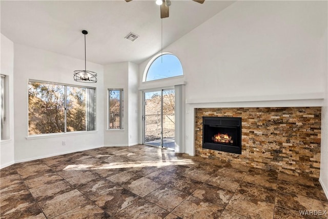 unfurnished living room featuring visible vents, a high ceiling, a tiled fireplace, baseboards, and ceiling fan with notable chandelier