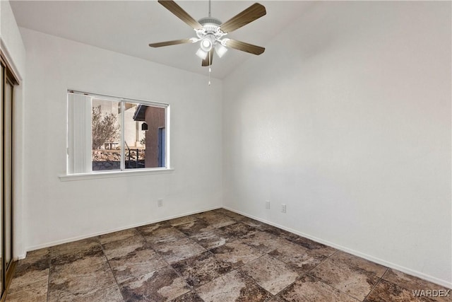 unfurnished room featuring lofted ceiling, stone finish floor, baseboards, and a ceiling fan