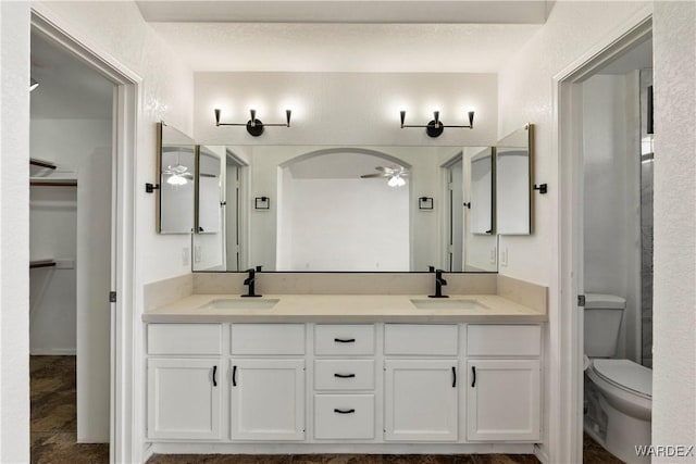 full bathroom featuring ceiling fan, double vanity, a sink, and toilet