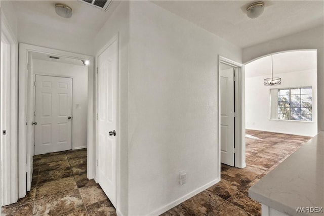 corridor featuring arched walkways, stone finish floor, visible vents, and baseboards